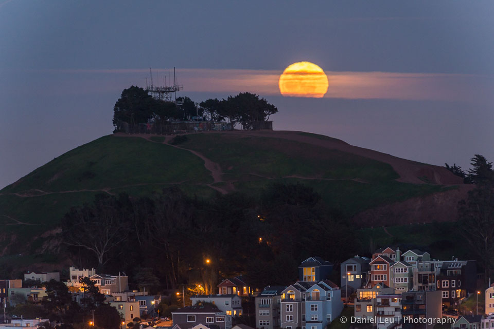 The rising full moon covered by some clouds behind the Bernal Heights Park peak.